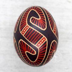 an ornately decorated egg with the letter s painted on it's side, sitting on a white surface