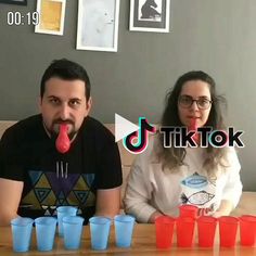 two people sitting at a table with plastic cups in front of them and one person sticking his tongue out