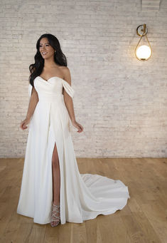 a woman in a white dress standing on a wooden floor next to a brick wall