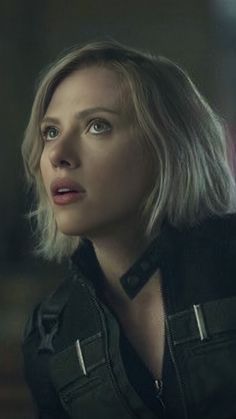 a woman with blonde hair and black jacket looking off to the side in a dark room