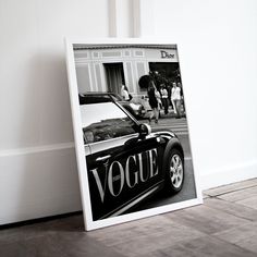 a black and white photograph of a car parked in front of a building with the word voque written on it