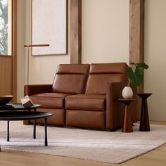 a brown leather couch sitting in a living room next to a coffee table and vase