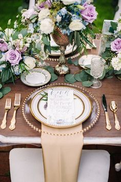 the table is set with plates, silverware and purple flowers on top of it