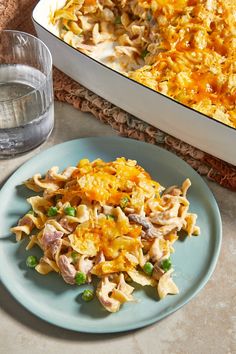 a blue plate topped with pasta next to a casserole dish filled with chicken