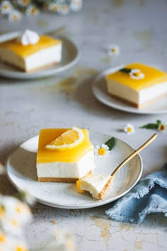 two slices of lemon cheesecake on white plates with flowers in the backgroud