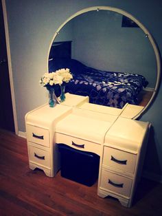 a white vanity with drawers and a mirror on the wall next to it, in front of a bed