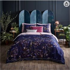 a bed with purple and pink comforters in a room next to potted plants