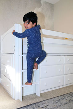 a little boy standing on top of a white bunk bed