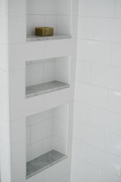 three shelves in the corner of a white tiled bathroom