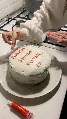 a woman cutting a cake on top of a white counter next to a red marker