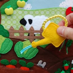 a hand is holding a piece of felt that has been made to look like a farm scene