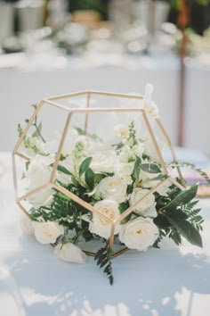 white flowers are in a geometric vase on a blue table cloth with greenery and candles