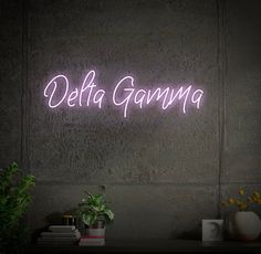 a neon sign that reads delta gammya on the wall next to a potted plant