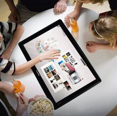 four people sitting at a table with an ipad in front of them holding drinks and snacks