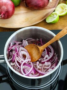 onions and limes are being cooked in a pot on the stove top with a wooden spoon