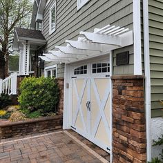 a garage with a white pergolated roof and brick walkway leading to the front door