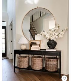 an entryway with baskets and a mirror on the side table next to a staircase