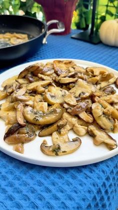 a plate full of mushrooms sitting on a blue table cloth next to a skillet