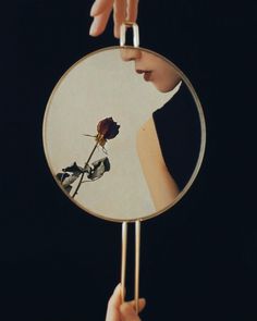 a person holding a mirror with a reflection of a rose in it's center