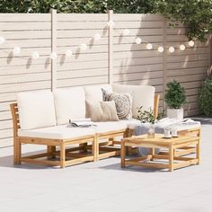 an outdoor seating area with white cushions and lights strung over the fence behind it,