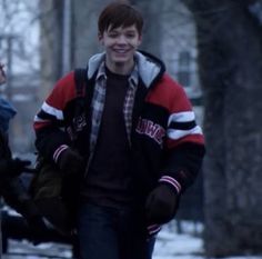 two young men are walking down the street in the snow, one is wearing a red and black jacket