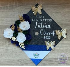 a graduation cap decorated with flowers and butterflies on top of a wooden table next to a flag