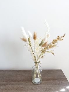 a glass vase filled with white flowers on top of a wooden table next to a wall