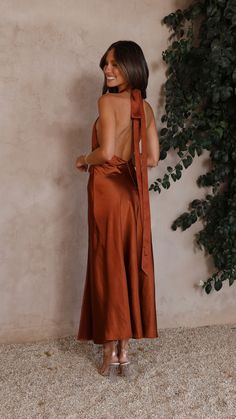 a woman standing in front of a plant wearing an open back dress