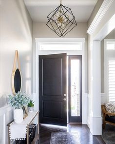 an entryway with a black door and white trim on the walls, along with a gold framed mirror