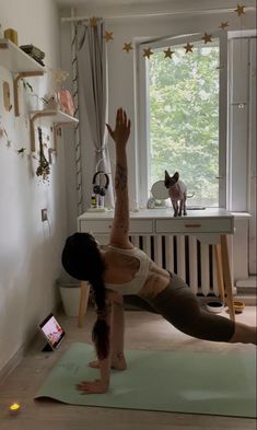 a woman is doing yoga in front of a window with her dog on the other side