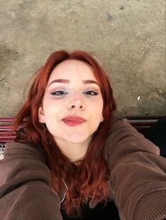 a woman with red hair and blue eyes is taking a selfie while sitting on a bench