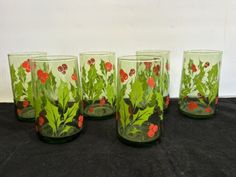 four green glasses with red flowers and leaves painted on the glass are sitting on a black surface