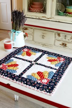 a quilted table runner on top of a white counter with a vase and flowers