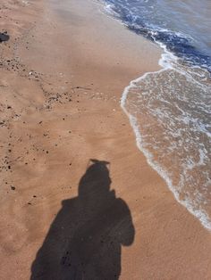 a shadow of a person on the beach next to the water and sand with waves coming in