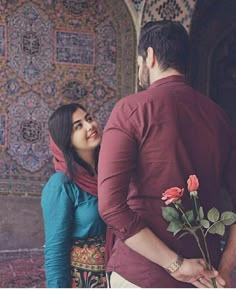 a man and woman standing next to each other near a wall with flowers in it