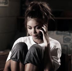 a woman sitting on a bed talking on a cell phone while holding her hand up to her ear