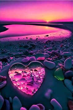 a heart shaped object sitting on top of a beach next to the ocean at sunset