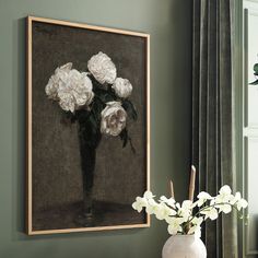 a vase filled with white flowers on top of a table next to a wall mounted painting