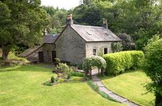 an aerial view of a stone house surrounded by trees and shrubs, with a path leading to the front door