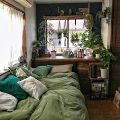 a bed with green sheets and pillows in front of a window filled with potted plants