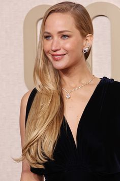 a woman with long blonde hair wearing a black dress and diamond necklace smiling at the camera