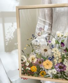 a person holding up a wooden frame with flowers in it