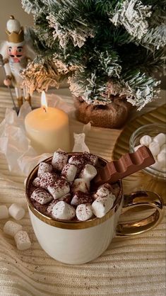 a cup filled with marshmallows next to a small christmas tree and candle