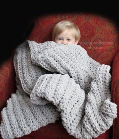 a little boy wrapped in a blanket on top of a red chair with his eyes closed