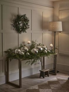 a table with candles and greenery on it next to a wall decorated with wreaths