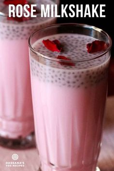 two glasses filled with pink milkshake on top of a wooden table next to each other