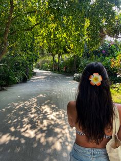 a woman with a flower in her hair walking down a road surrounded by trees and bushes