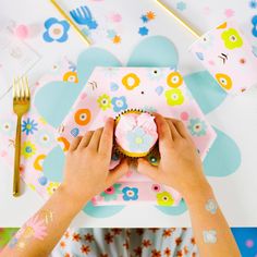 a person holding a cupcake on top of a pink and blue place mat with flowers