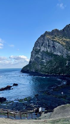 people are standing on the edge of a cliff overlooking the ocean and rocky coastline with mountains in the background