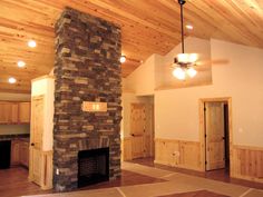 an empty living room with wood paneling and a stone fire place in the center